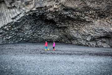 Women walking on black sand under basalt columns in Iceland