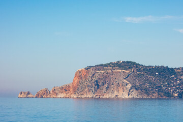Fototapeta na wymiar The Alanya Peninsula with old city fortress. View from the beach with calm sea