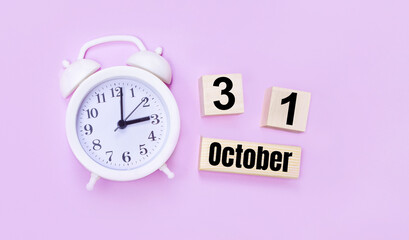Two wooden cubes and a block with the text OCTOBER 31 and a white alarm clock on a light pink...