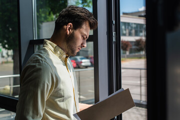 Side view of businessman looking at paper folder near window in office.