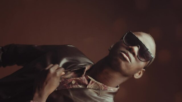 Rotating studio portrait of self-confident African American man wearing fashionable outfit with eyeglasses posing on camera