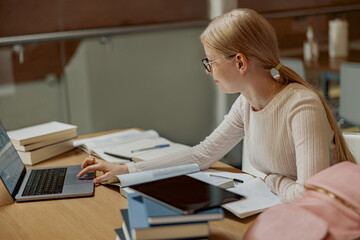 Young talented female student studying in university library use laptop and books