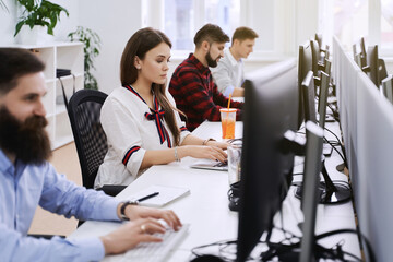 People working in modern IT office. Group of young and experienced programmers and software developers sitting at desks working on computers. Team at work.