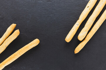 Fresh Italian Grissini Breadsticks served on black background. Dry baked bread with olive pieces on slate plate. Top view, copy space