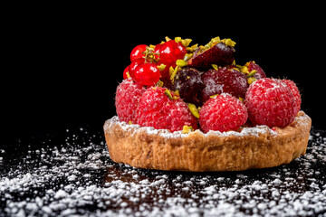 A very nice fruit tart on a black background. Powdered sugar is placed on the black support