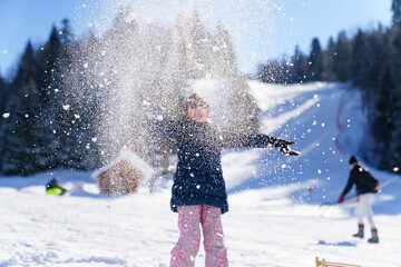 Happy child throwing snow on air. Sunny winter holidays outdoor. Kid having fun at snowy ski resort, enjoying Christmas vacation in mountains. Snowflake like magical glitter. Candid lifestyle moment