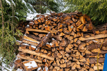 A lot of chopped and piled-up wood outdoors, covered with snow in winter 