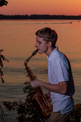A young guy plays the saxophone in the evening at sunset