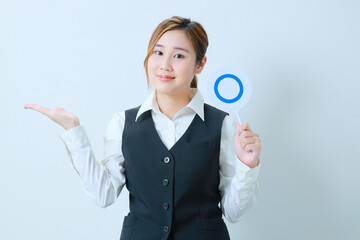 左手に○プレートを持ち右手を広げるOL