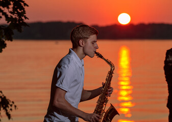 A young guy plays the saxophone in the evening at sunset