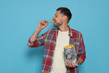 Handsome man eating potato chips on light blue background