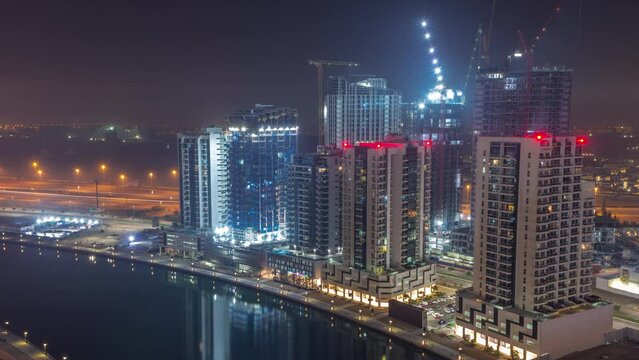 Towers at the Business Bay during all night timelapse in Dubai, United Arab Emirates. Construction site aerial view from above with canal