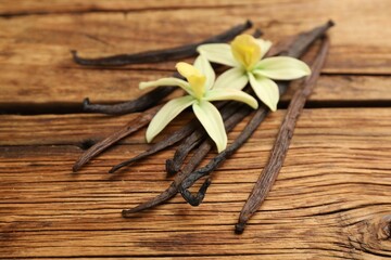 Fototapeta premium Aromatic vanilla sticks and flowers on wooden table, closeup
