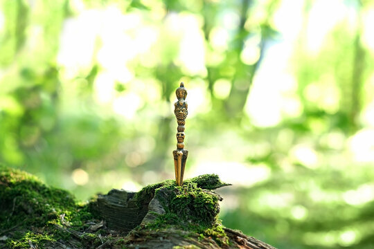 Ritual knife on mossy stump, blurred natural green background. Phurba is a three-sided knife, implement traditionally of Indo-Tibetan Buddhism. used for magic practice, esoteric spiritual ritual