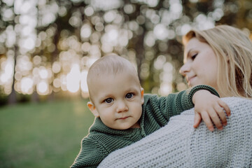 Mother holding her little baby son wearing knitted sweater during walk in nature.