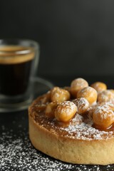 Delicious tart with hazelnuts, sweet caramel and powdered sugar on black table, closeup