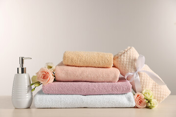 Fototapeta na wymiar Soft towels, dispenser, roses and eustoma flowers on light wooden table