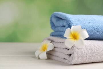 Obraz na płótnie Canvas Closeup view of soft folded towels and plumeria flowers on white wooden table, space for text