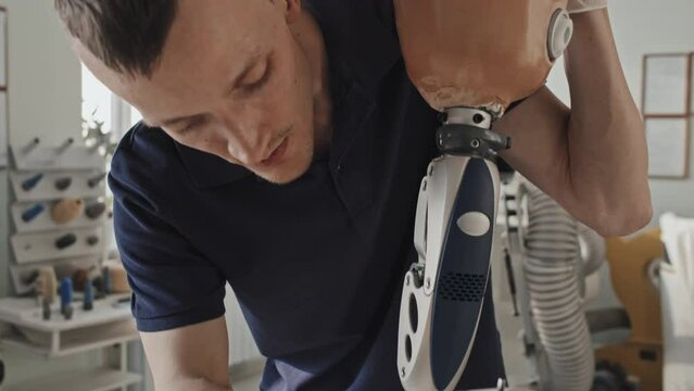 Tilt down shot of modern professional craftsman assembling and fixing parts of leg prosthesis in his workshop