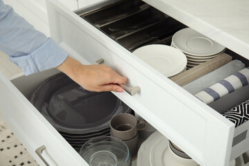 Woman opening drawer of kitchen cabinet with different dishware and towels, closeup