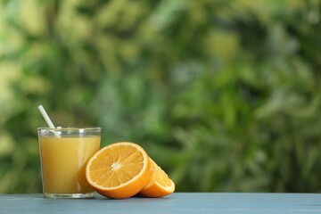 Delicious orange juice and fresh fruit on light blue wooden table against blurred background. Space for text