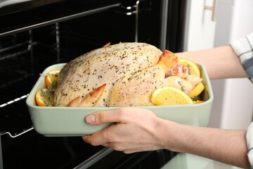 Woman putting raw chicken with orange slices into oven, closeup