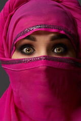 Close-up shot of a young charming woman wearing the pink hijab decorated with sequins. Arabic style.