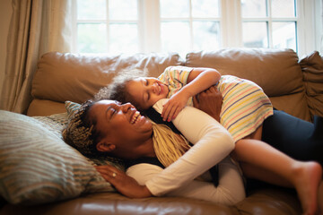 Happy playful mother and daughter on living room sofa