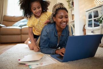 Happy daughter watching mother work at laptop on living room floor