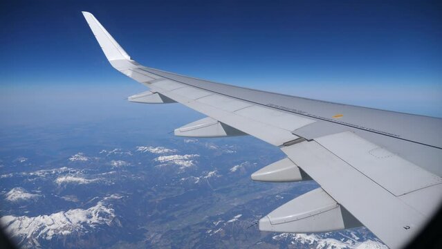 View from passenger cabin window of wing of aircraft flying over Austrian Alps on sunny day against background 
