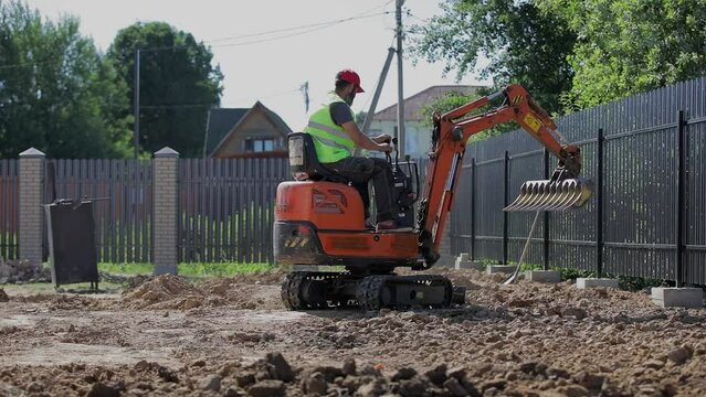 A man on a mini-excavator levels a piece of land, loosens the soil