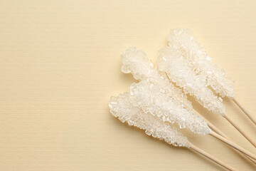 Wooden sticks with sugar crystals and space for text on beige background, flat lay. Tasty rock candies