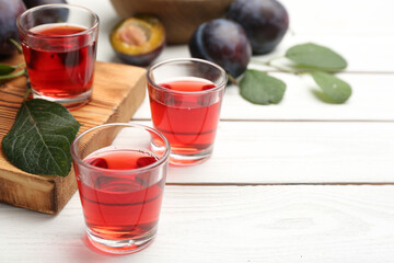 Delicious plum liquor and ripe fruits on white wooden table, space for text. Homemade strong alcoholic beverage