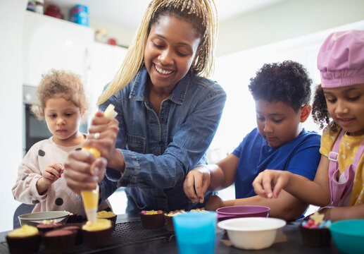 Happy mother and kids decorating cupcakes in kitchen