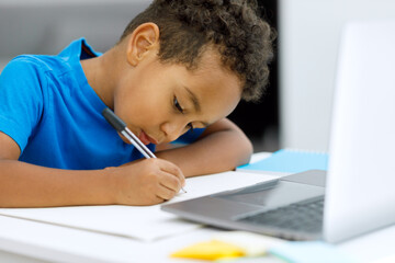 Focused black guy with a laptop sitting at the table too close to the notebook, side view.