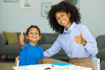 Image of a young female teacher showing thumbs up along with her student sitting in a classroom