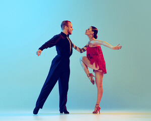 Naklejka premium Dynamic portrait of professional dancers in stage attires dancing ballroom dance isolated on blue background. Concept of art, beauty, music, style.
