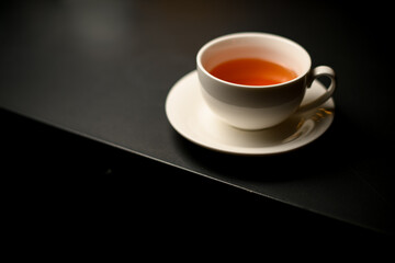 Beautiful white porcelain cup of tea and saucer on black table