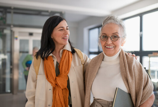 Happy mature woman student with book discussing with teacher in corridor in university.