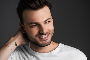 Portrait of brunette man smiling and looking away isolated on grey.