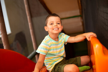 Cheerful smiling six-year-old boy in the children's play center on the top of the slide - 523526623