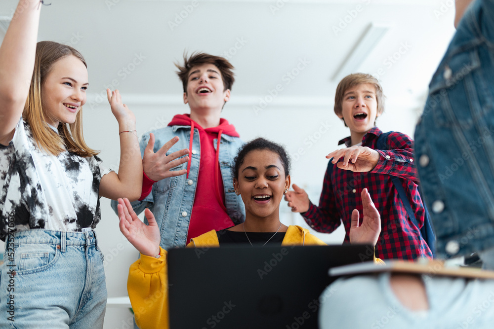 Sticker high school students sitting together at desk and using laptop and talking during break in classroom