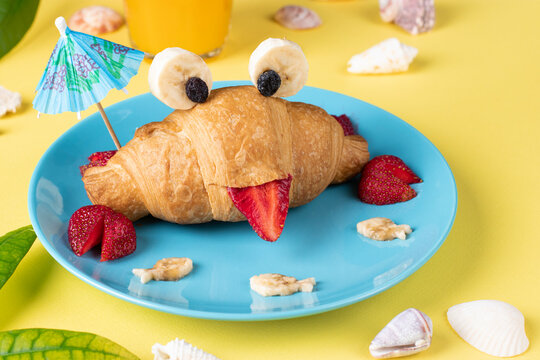 Naklejki Fun food for kids - crab shaped croissant with strawberry and banana on yellow background