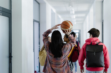 Rear view of young high school students walking in corridor at school with basketball ball, back to school concept.