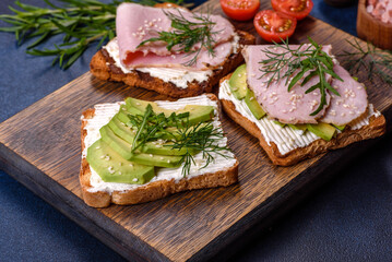 Fresh, delicious ham, butter, avocado and sesame seeds sandwiches on a wooden cutting board