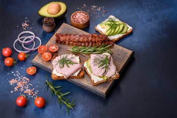 Fresh, delicious ham, butter, avocado and sesame seeds sandwiches on a wooden cutting board