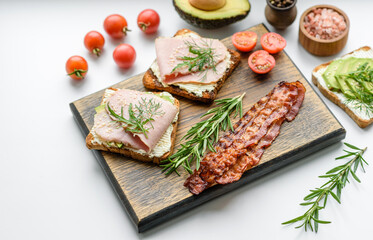 Fresh, delicious ham, butter, avocado and sesame seeds sandwiches on a wooden cutting board