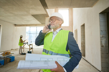 Foreman holds folded drawings and speaks on mobile phone