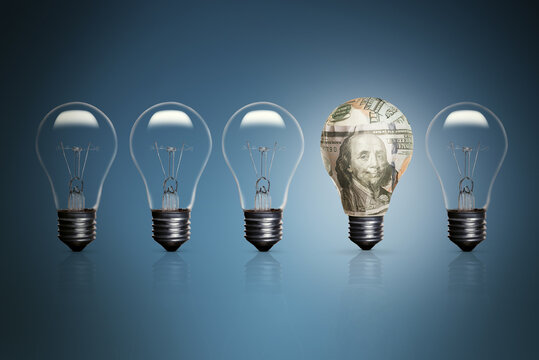 Five lightbulbs on a blue background and one of them wrapped with 100 dollars