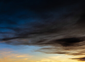 Gloomy clouds creep over the sunny sunset sky